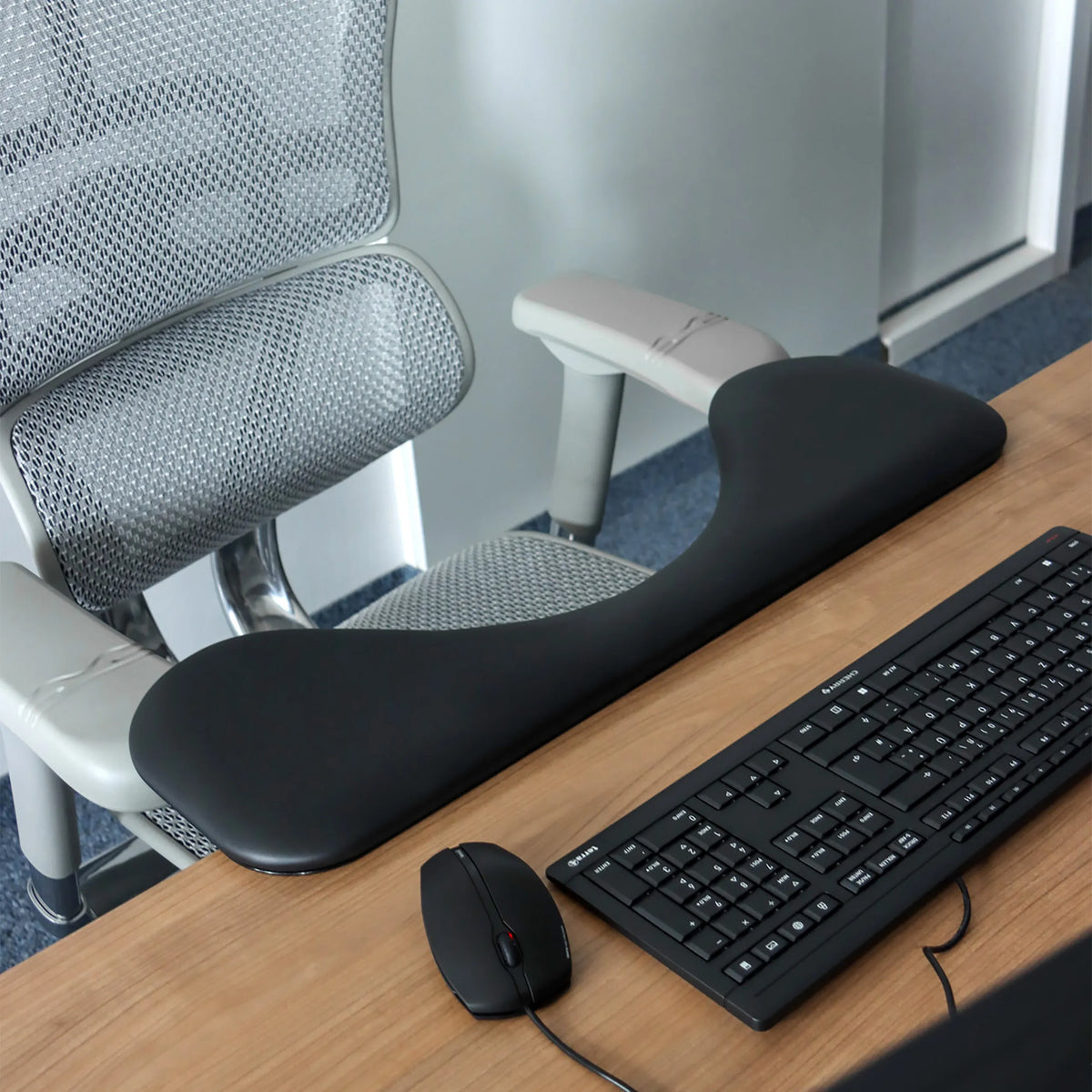 Black RELEX RT2 armrest on a desk next to a keyboard and a computer mouse by hjh OFFICE