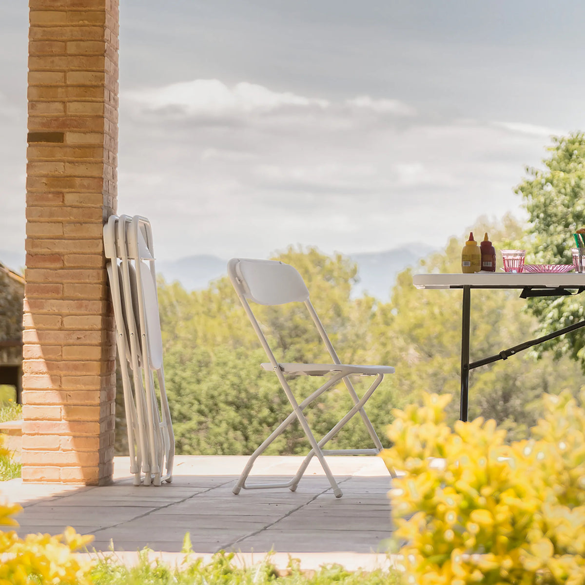 White outdoor chair TUDELA XXL W in an outdoor view next to a folding table by hjh OFFICE