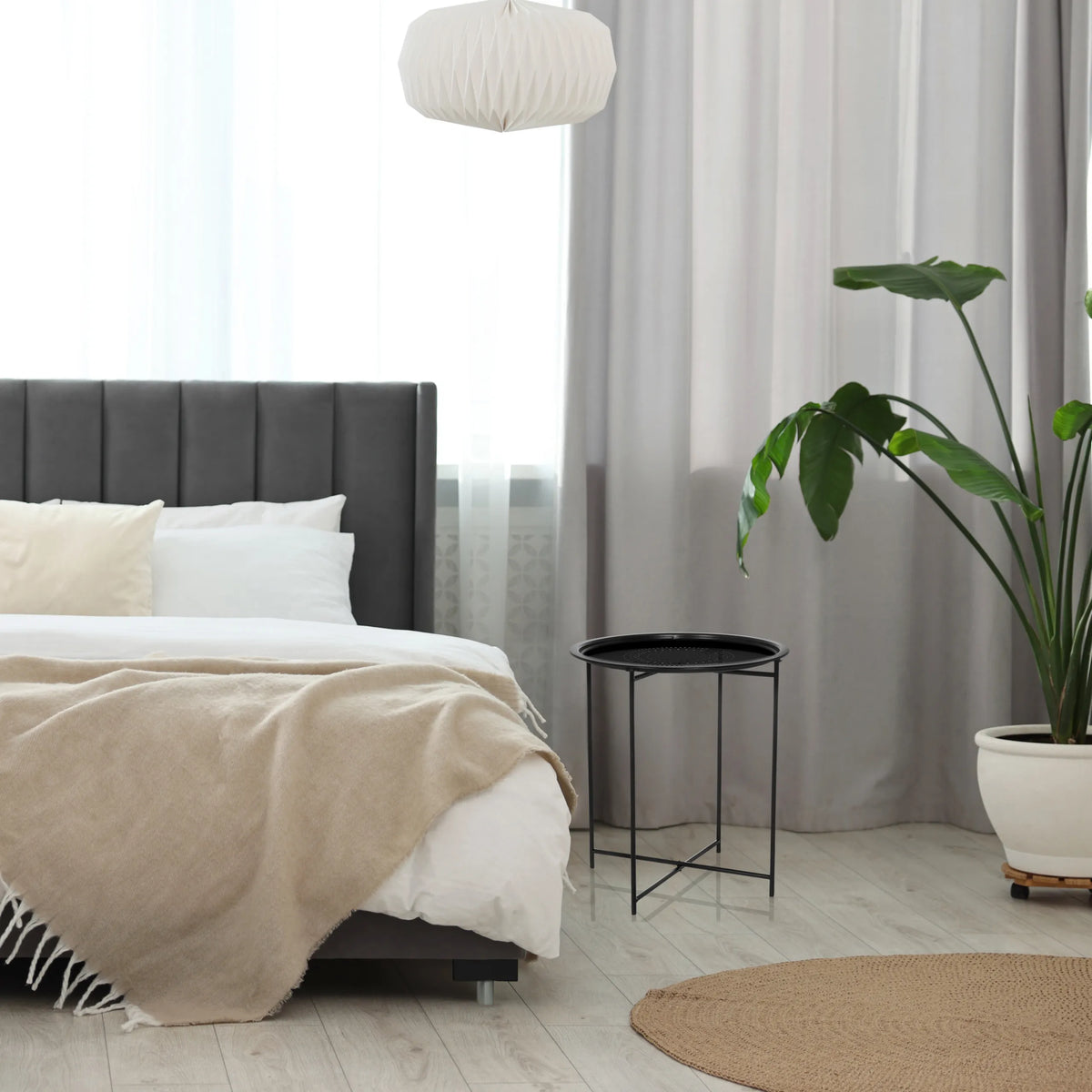 Black ALLRUND metal side table with a perforated top next to a bed by hjh LIVING