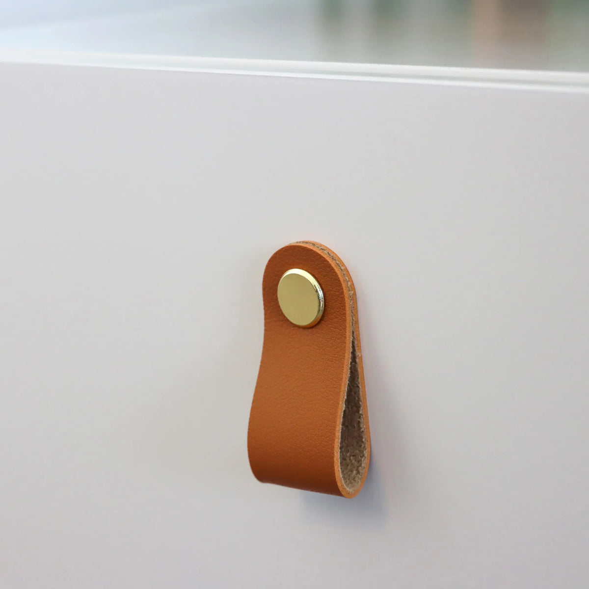Brown leather handle with gold-coloured button on the white side table TAROLO III by hjh LIVING