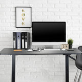 Black standing desk STAND CR with monitor, keyboard and ring binders in front of a white brick wall by hjh OFFICE