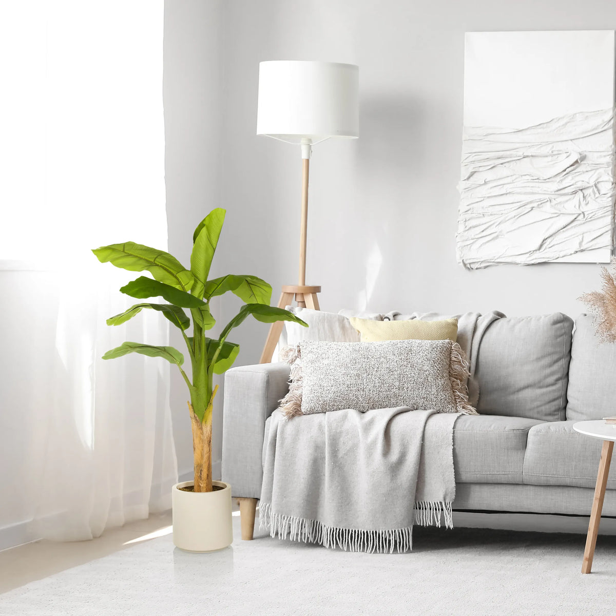 Green artificial plant BANANE I in a light-coloured pot next to a grey sofa by hjh OFFICE
